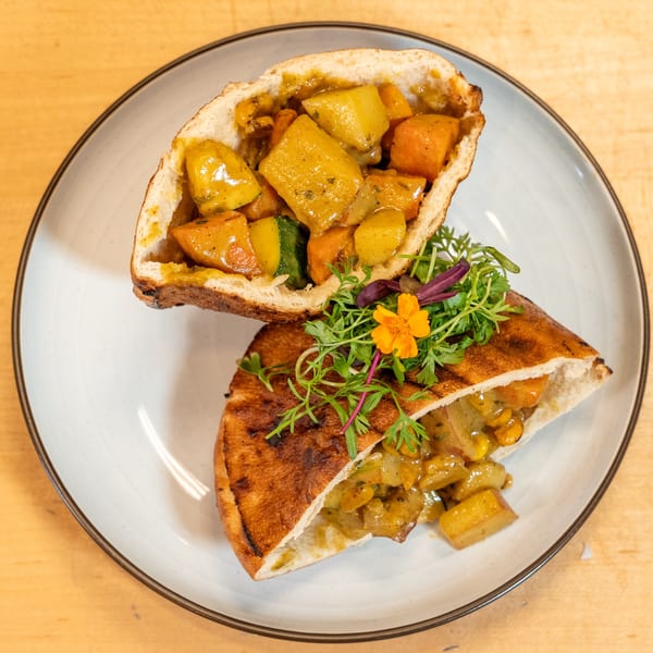 Two halves of pita bread filled with Caribbean vegetable curry, garnished with microgreens and an orange flower.