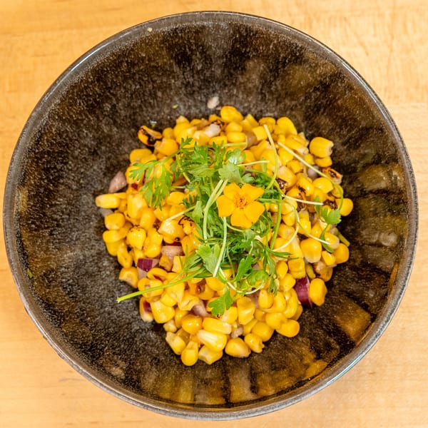 Manjay Restaurant's corn dish with red onions, cilantro, and an edible yellow flower in a dark bowl.