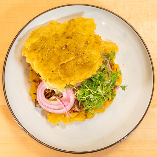 A Manjay Restaurant Caribbean sandwich with plantain buns, shredded meat, red onions, and microgreens.