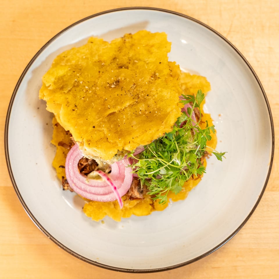 A Manjay Restaurant Caribbean sandwich with plantain buns, shredded meat, red onions, and microgreens.