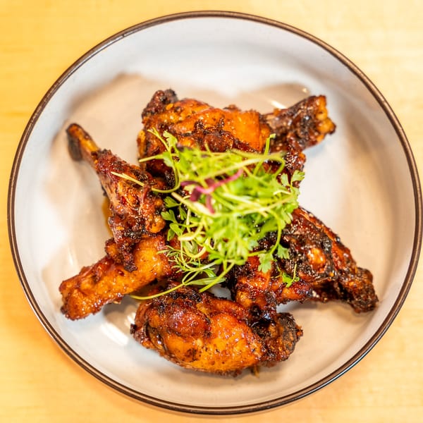 A white bowl filled with glistening, dark Caribbean chicken wings garnished with fresh green herbs.
