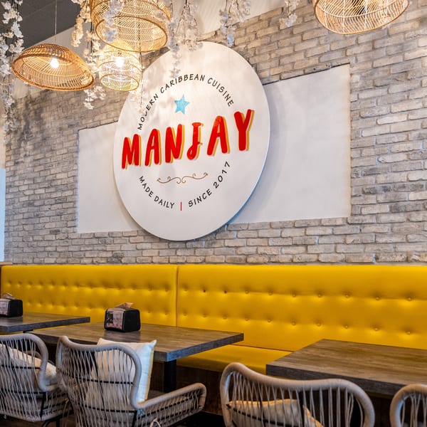 Manjay Restaurant's interior with a large circular logo, yellow booth seating, and woven light fixtures.