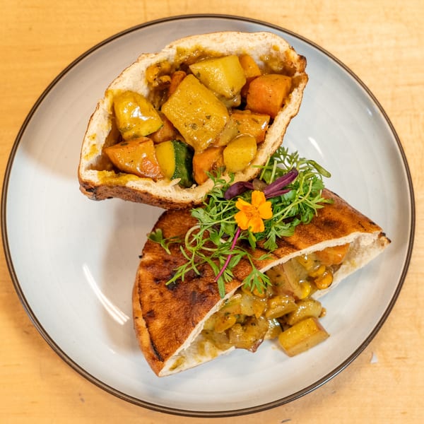 Two halves of a Caribbean curry vegetable roti, garnished with greens and an orange flower.