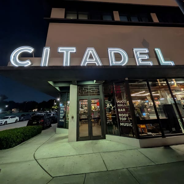 Exterior of Citadel food hall at night, with glowing white sign and glass entrance.