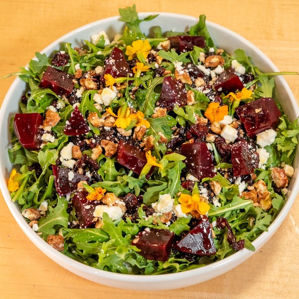 A vibrant salad with arugula, diced beets, feta cheese, walnuts, dried cranberries, and edible yellow flowers.