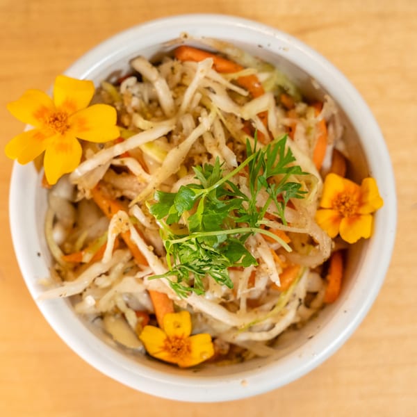 Manjay Restaurant's Caribbean coleslaw with shredded cabbage, carrots, and parsley, garnished with yellow flowers.