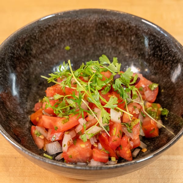 Close-up of a black bowl filled with diced tomatoes, onions, and fresh green herbs.