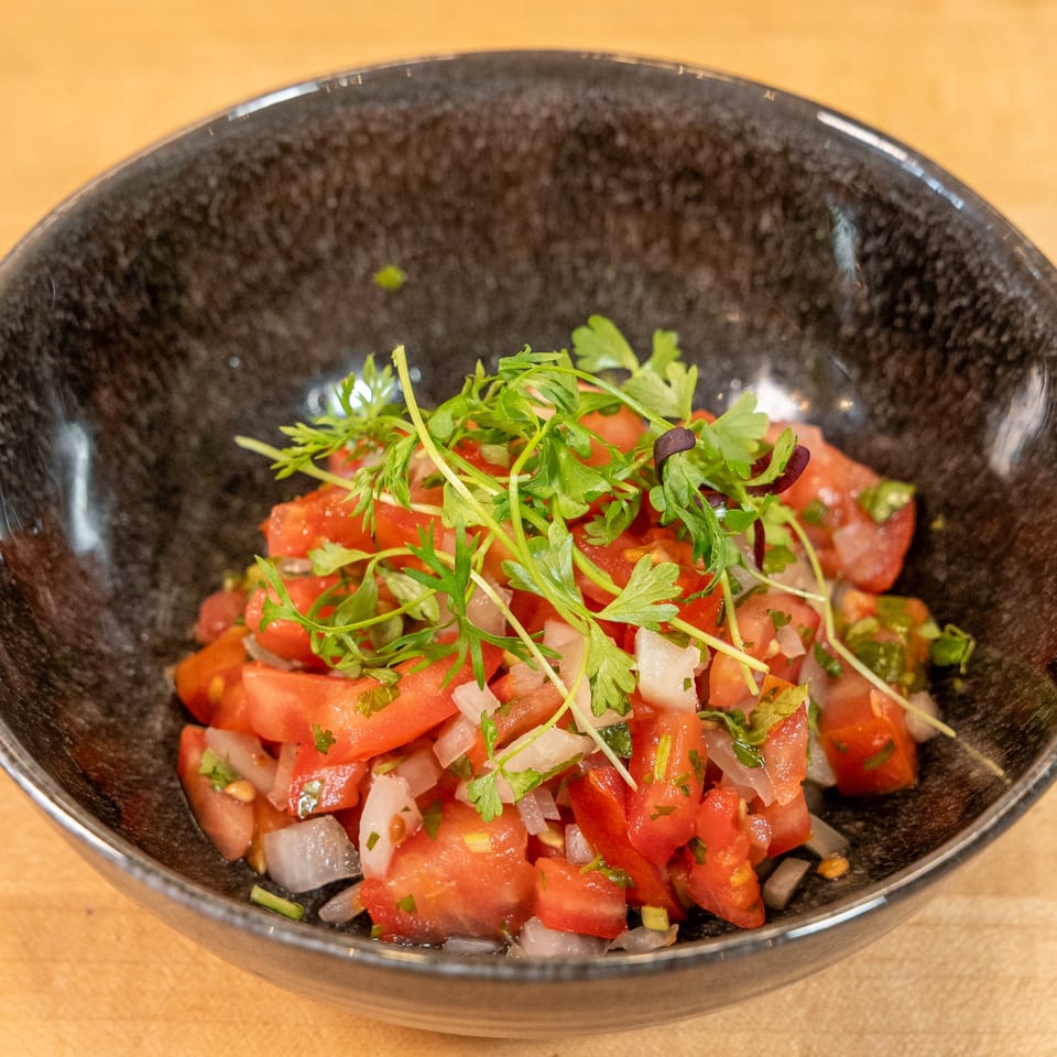 Close-up of a black bowl filled with diced tomatoes, onions, and fresh green herbs.