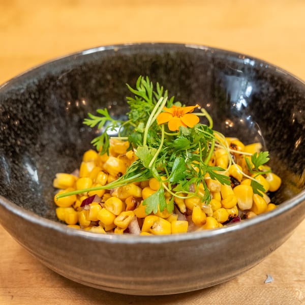 Manjay Restaurant's grilled corn salad with red onions, garnished with fresh herbs and an orange flower.