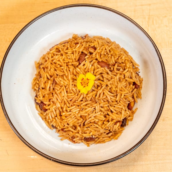 Manjay Restaurant's Caribbean rice and beans, garnished with a small yellow flower, on a white plate.
