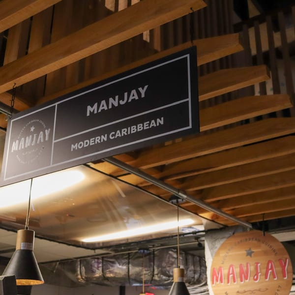 A black sign with "MANJAY MODERN CARIBBEAN" hangs from a wooden slatted ceiling.