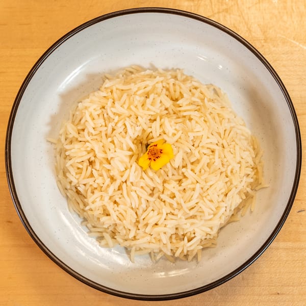 A white bowl filled with light brown rice, garnished with a single yellow and orange flower.