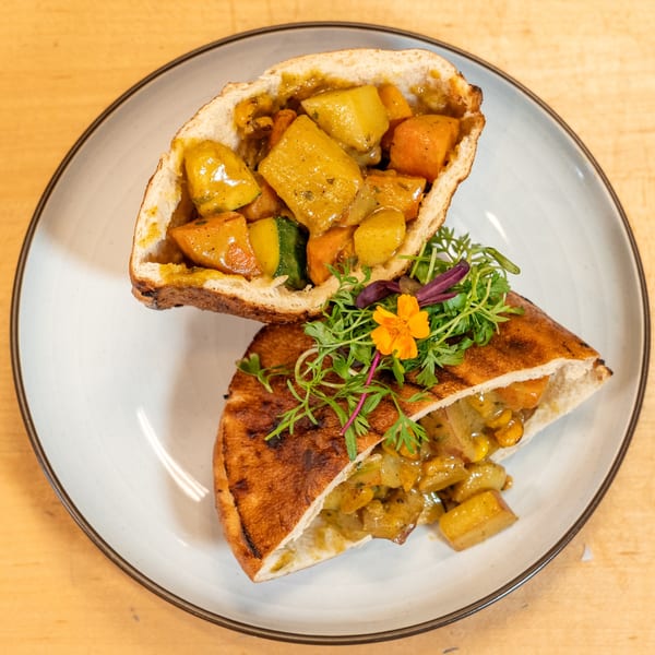 Manjay Restaurant's Caribbean vegetable curry in two pita halves, garnished with greens and an orange flower.